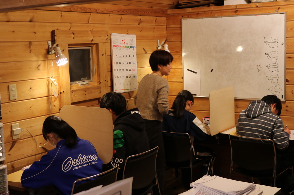 寺子屋きくち。茨城県ひたちなか市のアットホームな学習塾。先生が生徒の勉強の様子を見ている画像です。